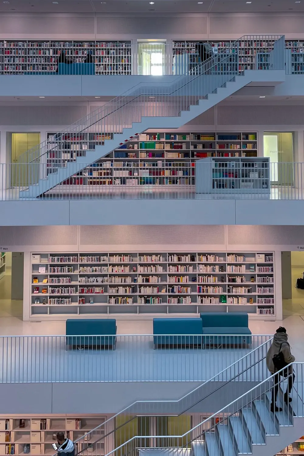 Bibliothèque sur plusieurs niveaux, rayonnages blancs et escaliers