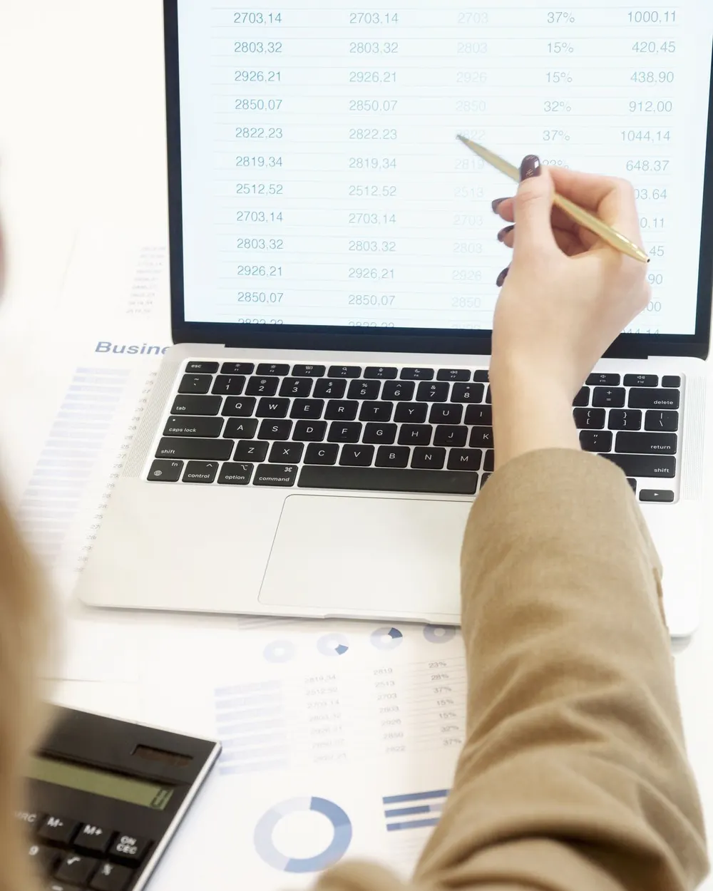 Reviewing a table of figures on a laptop, with a calculator and charts on the desk